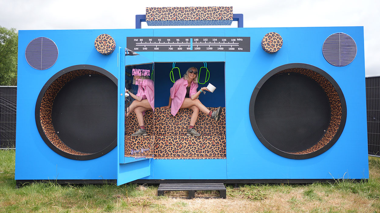 A WaterAid volunteer poses next to a bog in a boombox - a toilet housed behind the tape deck of a giant boombox, co-designed by Sir Rod Stewart and the charity - located near the Pyramid Stage at the Glastonbury Festival, at Worthy Farm in Somerset. Picture date: Wednesday June 25, 2025. (Photo by Yui Mok/PA Images via Getty Images)
